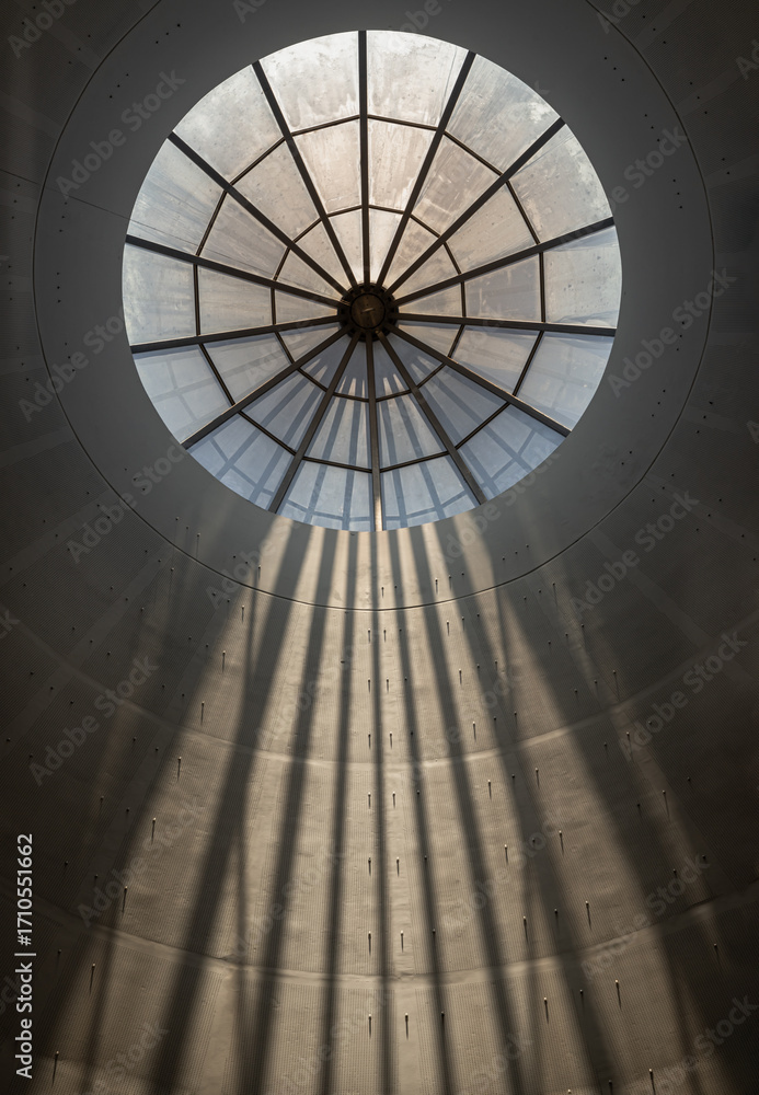 Fototapeta premium A decorative domed ceiling with prominent skylight is part of the interior architecture of Modern building. its iris diaphragm-like pattern and the way sunlight streams through it, creating visible ra