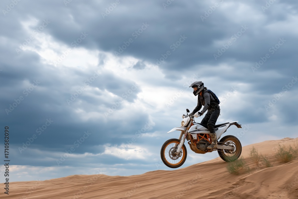Obraz premium Male riding motorcycle across desert sand dunes under cloudy sky adventure