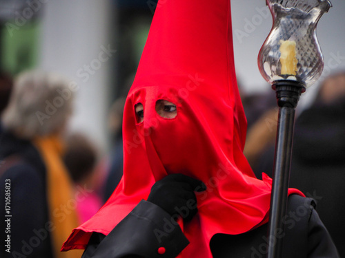 Religious Holy Week procession in Spain - A penitent or Nazareno in a red cape and a hood with a candle lantern, participating in a solemn Spanish tradition.