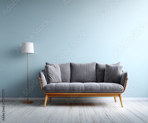 A light-filled room features a gray couch and a simple floor lamp against a pale blue wall, creating a tranquil and inviting atmosphere.