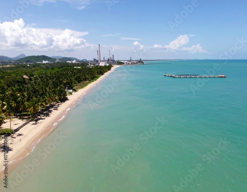 Coastal landscape with a beach, palm trees, and industrial buildings
