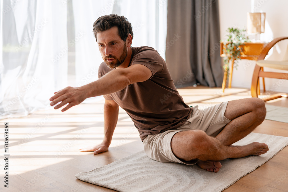 Fototapeta premium Man practicing yoga stretching on floor mat at home