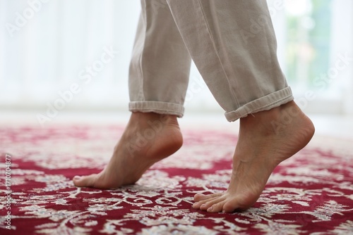 фотографія Woman walking barefoot on red carpet with pattern at home, closeup