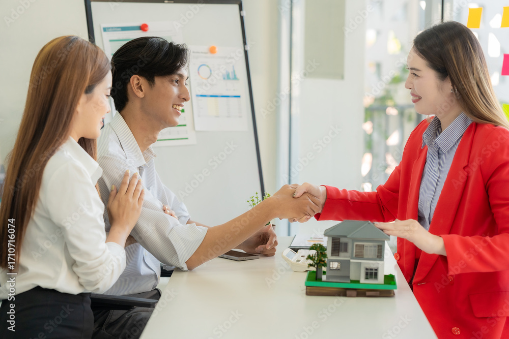 Fototapeta premium Closing the deal with paperwork and smiles. A couple shakes hands and thanks the real estate agent for the successful sale of their apartment, then concludes the deal and celebrates the purchase of th