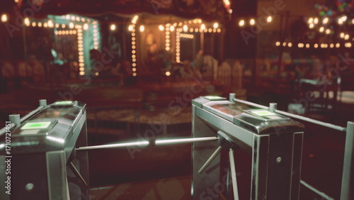 Canvas Print The entrance of an amusement park stands desolate at night, with turnstiles unoccupied and colorful lights casting a warm glow around