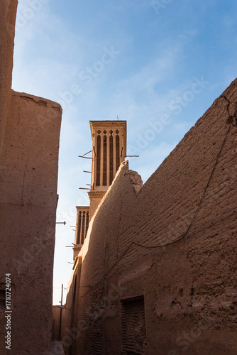 Traditional wind towers in Yazd's historic mud-brick alley, showcasing ancient Persian architecture under a clear blue sky. Ideal for travel, culture, and history themes.