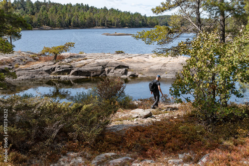 Back View of a Hiker Carrying a Knapsack and Walking Along the Rocky Shore of French River Ontario
