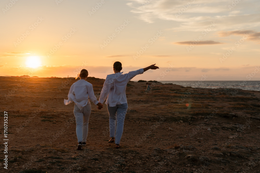 Fototapeta premium Couple Sunset Beach Walking - Silhouette of a couple walking hand in hand on the beach at sunset.