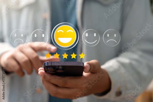 Satisfaction review, User giving five-star rating with happy emoji icon on smartphone screen, representing excellent customer feedback, digital reputation, and mobile user experience concept.