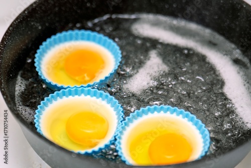 Wallpaper Mural Three poached eggs cooking in blue silicone molds in boiling water on a stove Torontodigital.ca