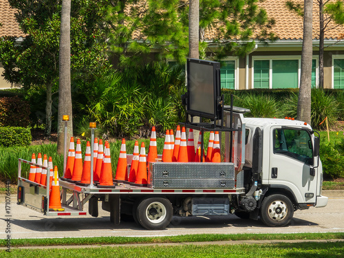 Orange traffic cones (for signaling temporary restrictions or hazards) below a truck-mounted message sign on a county public-works flatbed parked on a suburban parkway on a sunny afternoon in Florida