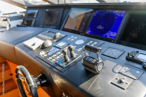 A close-up view of a yacht or ship bridge with the throttle controls. The navigation radar screen and electronic control panels are visible in the background