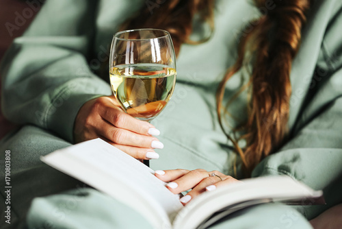 Woman relaxing with glass of wine and book. Cozy evening time at home in bedroom. Calm lifestyle with reading and drink. Female enjoying leisure in peaceful atmosphere. Rest after long day.
