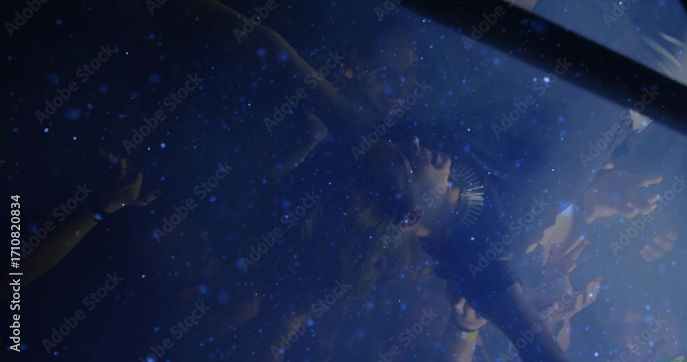 Fototapeta premium Lifting crowd surfer wearing spiked necklace at concert under blue lights, with confetti drifting