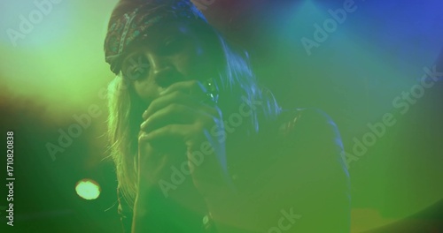 Singing female singer wearing patterned bandana on stage, with handheld microphone and haze