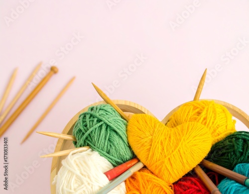 Colorful yarn balls and knitting needles in a heart-shaped basket on a pink background