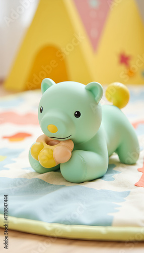 Cute green bear toy with yellow paws on colorful play mat  