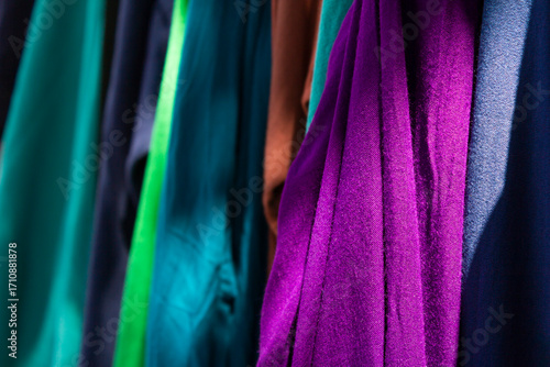 Colorful fabric textiles in vibrant shades of purple, teal, and blue hanging in a market display, perfect for fashion, sewing, and interior design concepts.