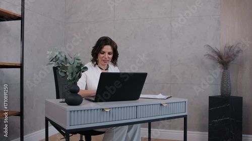typing laptop, stylish businesswoman, career woman, Stylish businesswoman in white outfit focused on her laptop, working at modern minimalist desk in professional office setting.