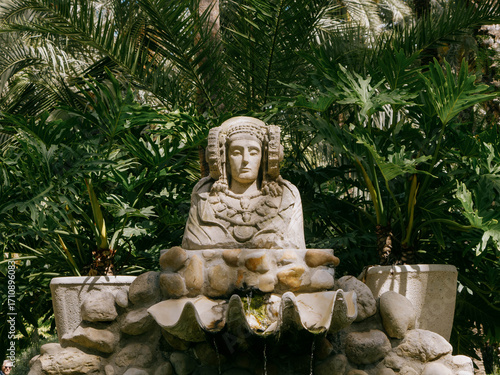 Busto de piedra de la Dama de Elche, entre palmeras, en entorno natural