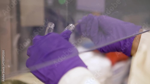 Close-up detailed view of a chemist using a small metal tool to move a substance from one small flask to another, before examining a reaction chamber — perfect for themes of chemistry, laboratory work
