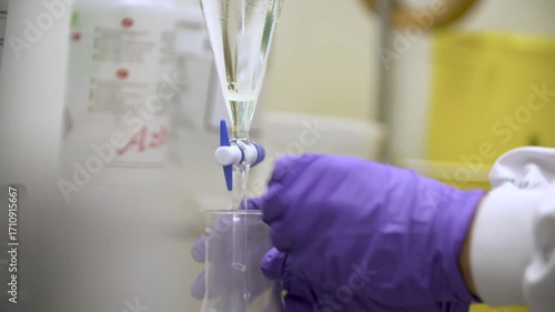 Close-up detailed view of a woman in laboratory attire pouring a substance from a pear-shaped funnel into a conical flask, gently shaking it as effervescence and gas form — themes of chemistry. 