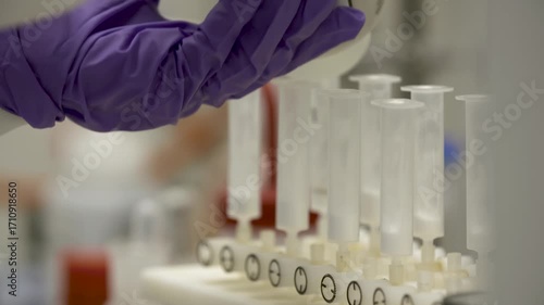 Close-up detailed view of a woman in lab wear carefully pouring equal small volumes of solvent from one bottle into multiple flasks —  themes of precision, accuracy, science, chemistry, method.