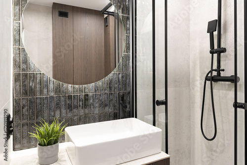 Modern bathroom interior with shower, white ceramic washbasin and dark tile on the wall with mirror. New apartment with elegant design.