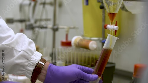Close-up detailed view of a woman in laboratory gloves carefully releasing orange liquid from a burette tap into a smaller container — perfect for themes of science, chemistry, precision, and analysis