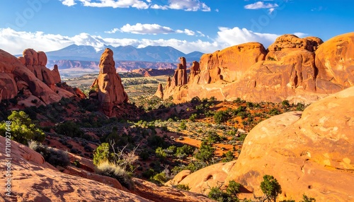 A vibrant landscape panorama showcases dramatic red rock formations and a distant mountain range under a partly cloudy sky.