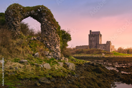 Sunset over historical Dunguaire Castle landmark in Kinvara, Galway Ireland with stone arch in foreground,  architecture background