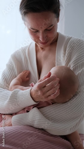 Vertical slow-motion closeup of a mother breastfeeding her infant daughter, gently cradling the babys head.