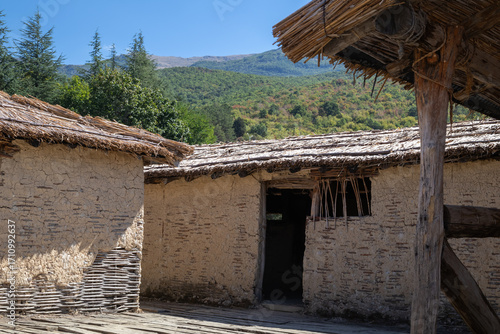a replica of a prehistoric village dwelling with mud walls and a thatched roof, showcasing ancient building techniques and a rustic, historical setting