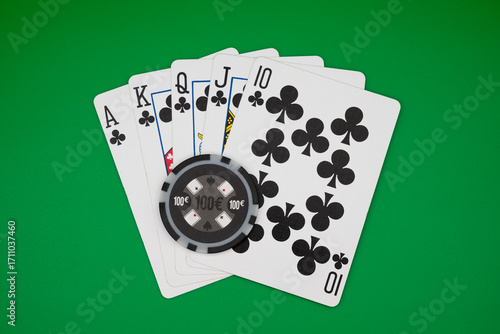 Obraz na plátne Royal flush in clubs with 100€ poker chip on green table, symbolizing ultimate poker hand, casino gambling, and high-stakes games