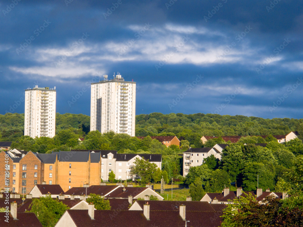 Fototapeta premium Multi-story residential buildings, apartments, townhouses, with varying architectural styles and colors. Green areas. High-rise residential tower blocks. Degree of landscaping or natural elements. 