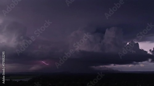 Dramatic storm clouds with lightning flash over a landscape.