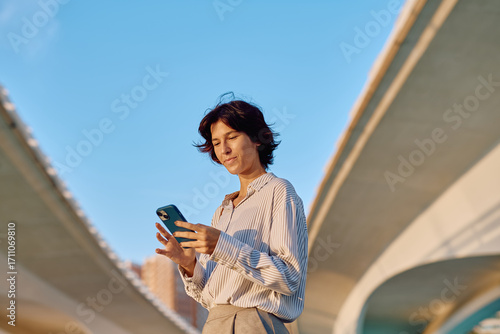 Cuadro en lienzo Businesswoman using a mobile phone app while sitting under a highway overpass in