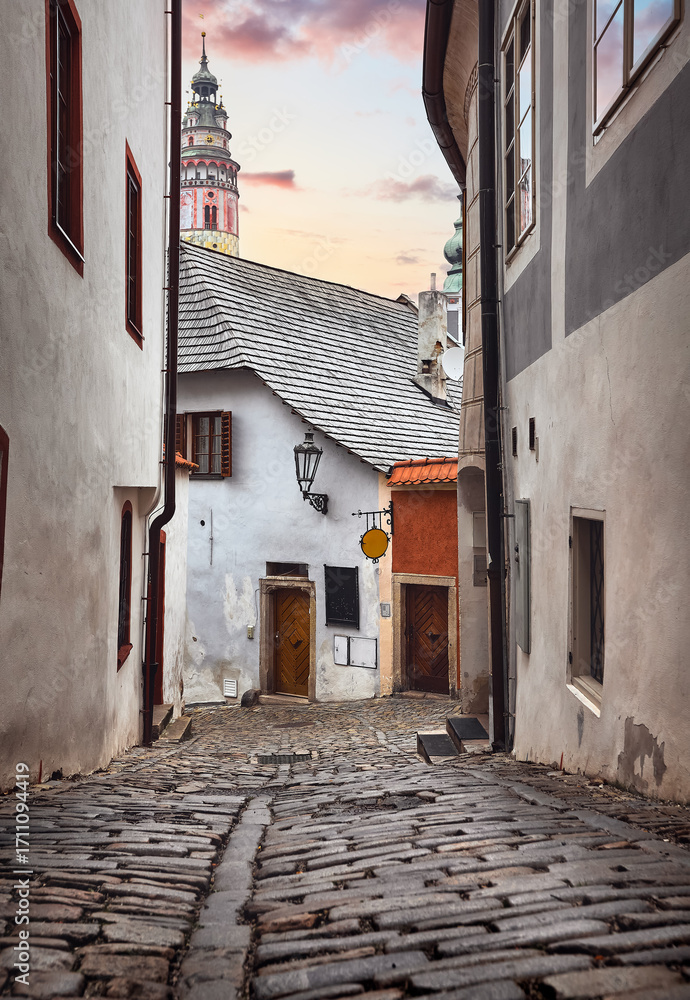 Obraz premium Cesky Krumlov (Czech Krumlov), Czech Republic. View at Castle Tower from the narrow street with medieval architecture in the ancient bohemian village with antique houses. Evening time romantic place.
