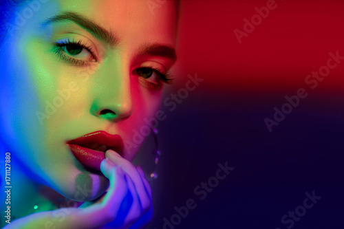 Beautiful young woman's face with perfect skin and colourful makeup in neon light. Color neon portrait of beauty model with makeup, long eyelashes and big pearl earrings. Selective focus. Close-up