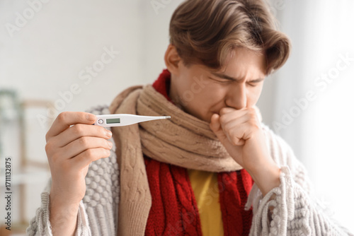 Ill young man with thermome...