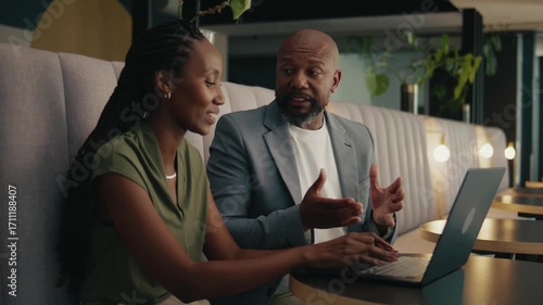 Black business colleagues discussing while using laptop sitting in office lobby