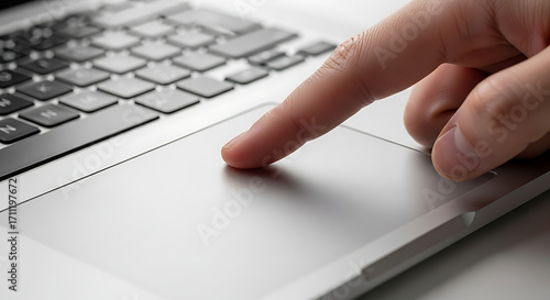 Finger touching a laptop touchpad with a keyboard visible in the background close up shot indoors