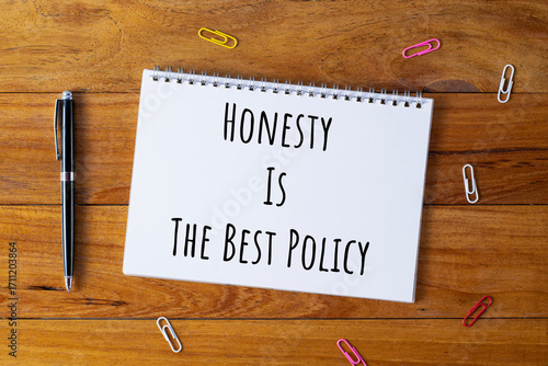 Selective focus of a pen, paper clips and notebook written with Honesty Is The Best Policy on wooden background.