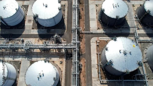 Aerial top down view of a large oil refinery and storage terminal with white fuel tanks and a complex pipeline network.