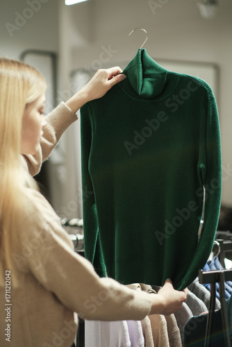 A girl tries on a striped sweater in a store. A young woman chooses clothes in a store while shopping. Seasonal holiday discounts on purchases. Black Friday
