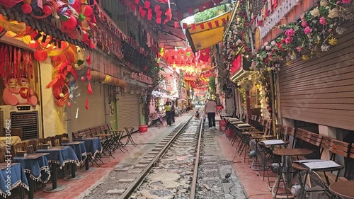 Morning view of the deserted Hanoi Train Street, Vietnam with railway tracks flanked by cafes and colorful lanterns.
