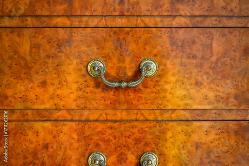 Close-up of Antique Dresser with Burl Wood Veneer and Ornate Brass Handle.