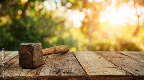 Rustic wooden table with a vintage hammer resting on its surface against a blurred nature background in soft sunlight