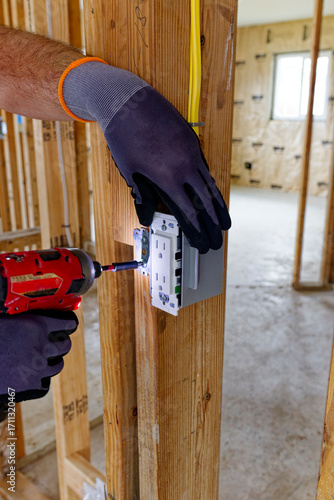 Electrician installing GFCI electrical outlet in wooden frame house, USA construction