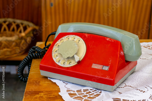 PRL interior with red rotary dial telephone, placed on wooden table covered with lace doily beside wicker basket.